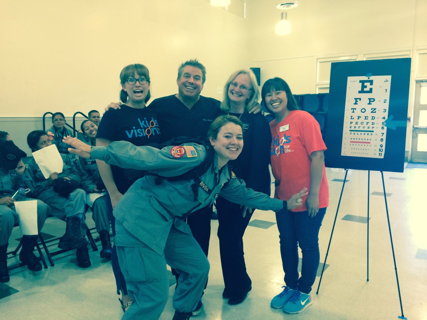 Steve Bender with Kids Vision for Life volunteers beside an eye chart at a vision screening for young cadets